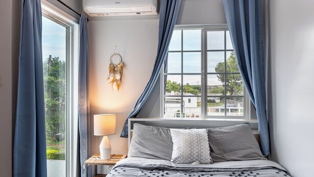 Une chambre avec une grande fenêtre, une lampe de chevet et un attrape-rêves accroché au mur.
