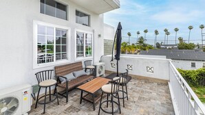 Une terrasse avec une table et des chaises en bois, un appareil de climatisation et une vue sur des palmiers.