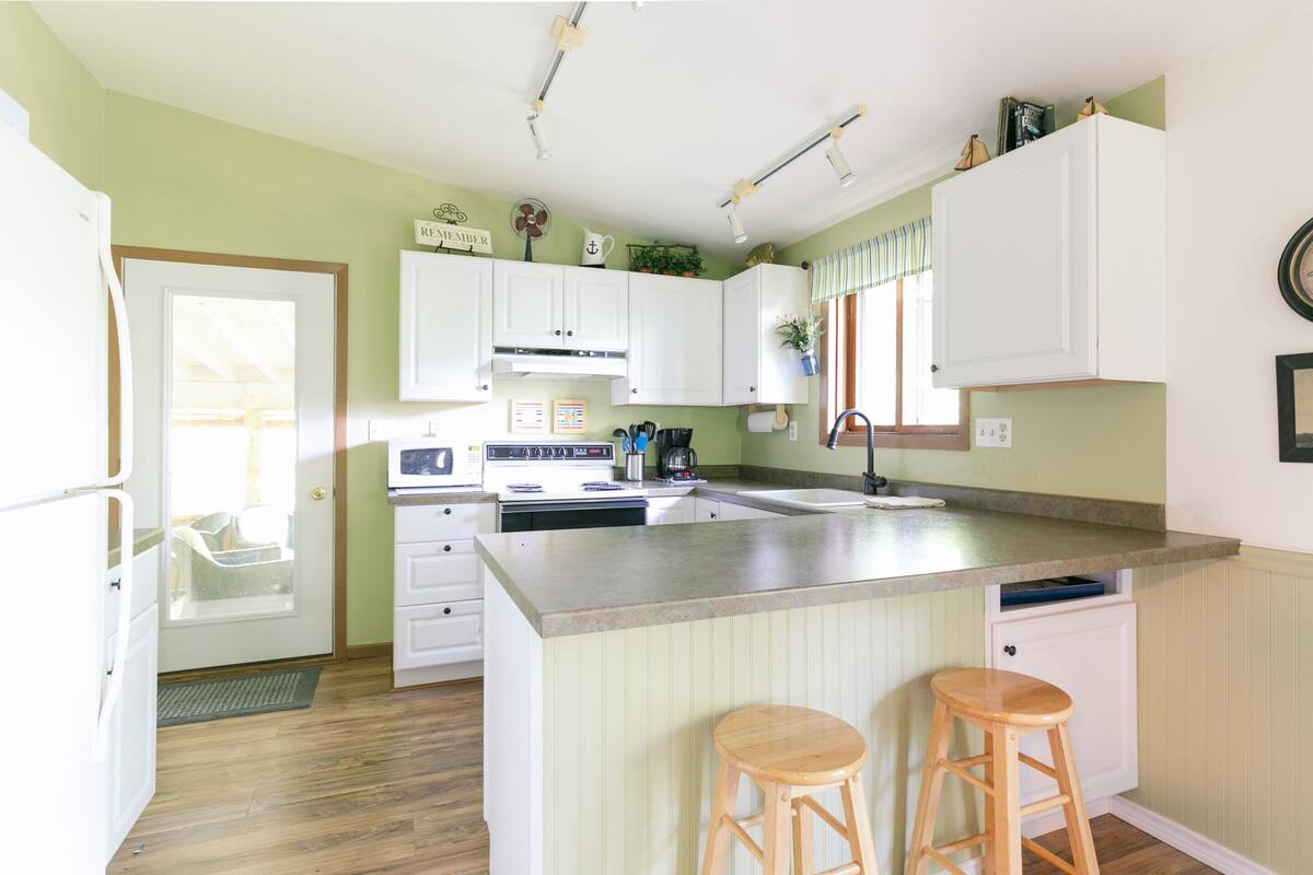 A kitchen with white cabinets, a large island with stools, a microwave, and a sink.
