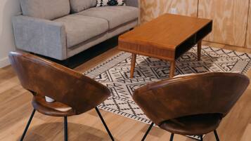 Una sala de estar moderna con un sofá gris, una mesa de centro de madera, dos sillones marrones y una alfombra estampada.