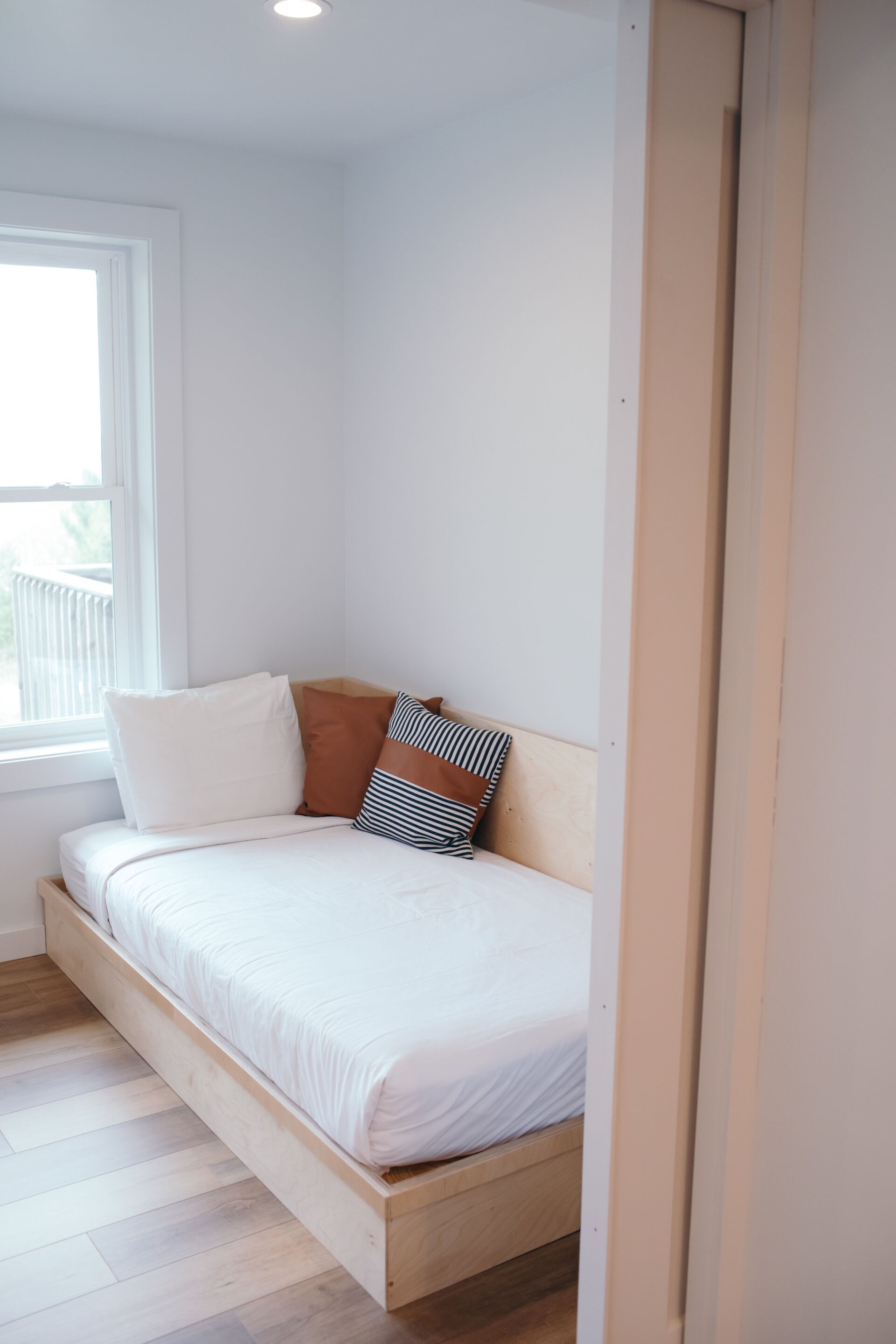 A single bed with a wooden frame, white bedding, and two pillows.