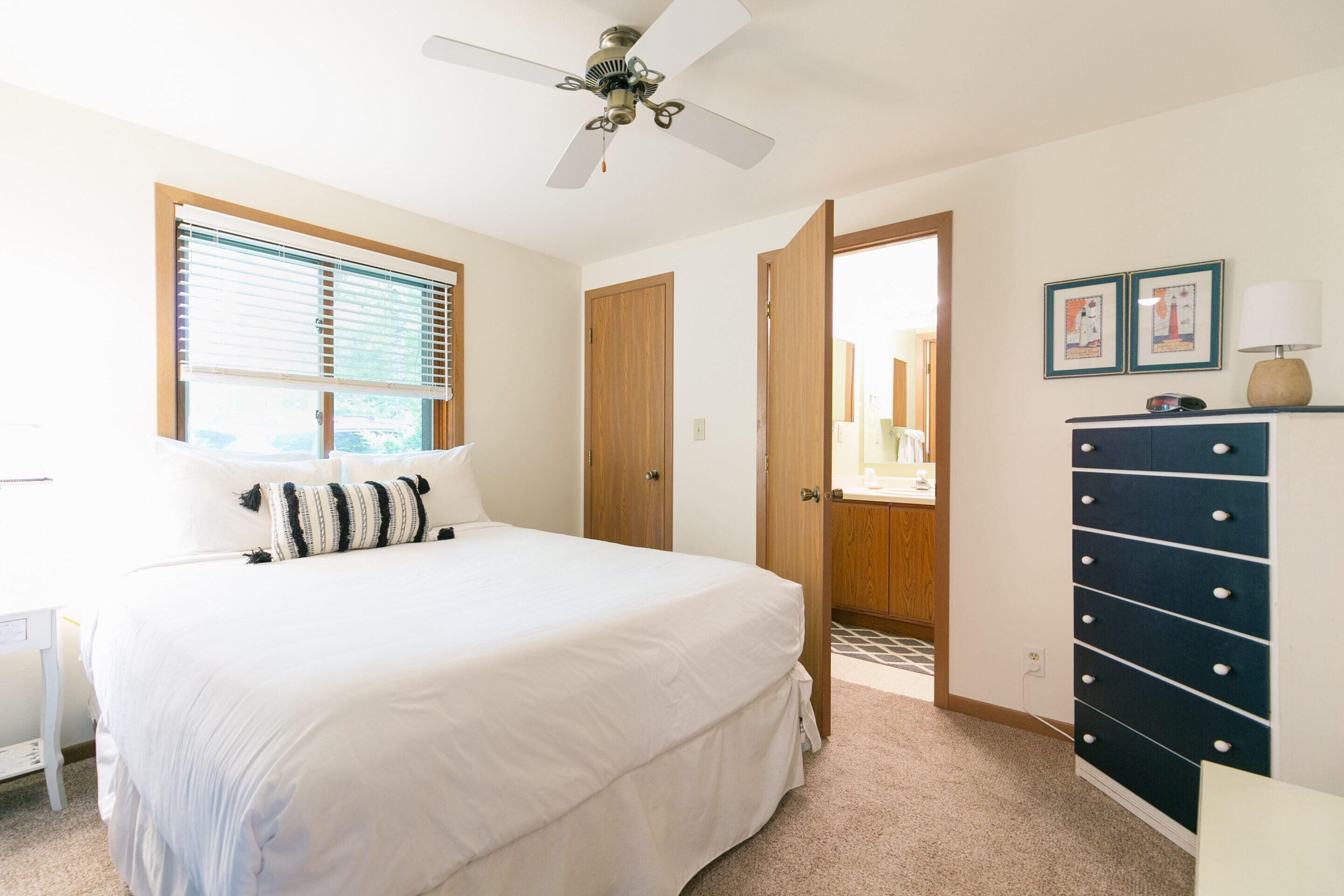A bedroom with a large bed, a ceiling fan, a dresser, and a door leading to another room.