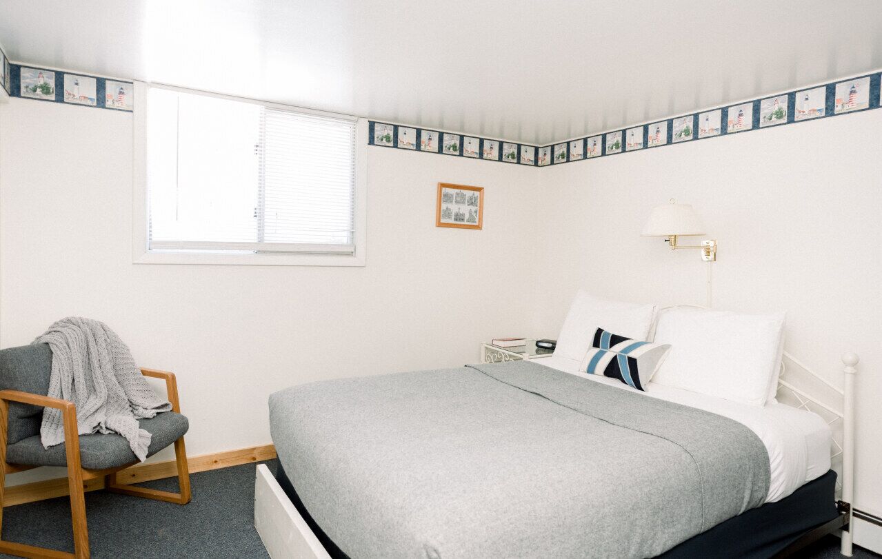 A bedroom with a bed, a chair, a nightstand, a lamp, and a window.