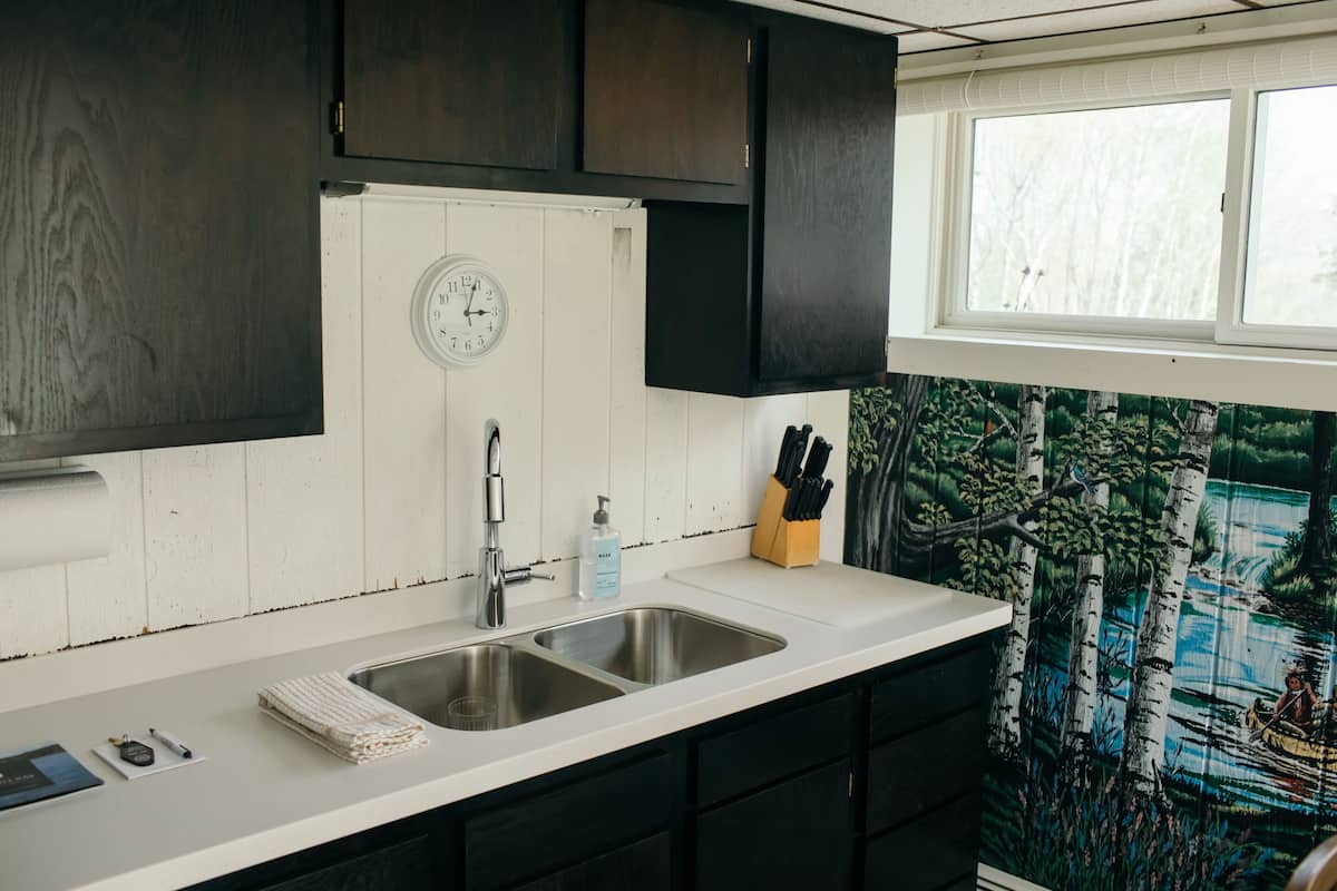 A kitchen with two sinks, a clock, a window, and a knife block.