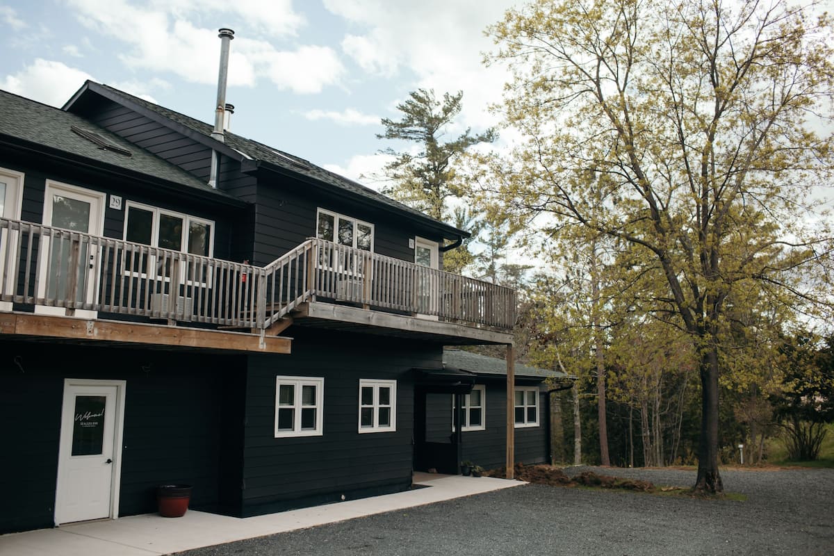 A two-story building with a balcony, a door labeled "Welcome," and a gravel driveway.