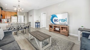Un saló modern amb zona de menjador, cuina de fons i un televisor que mostra 'BIG FISH Rentals'.