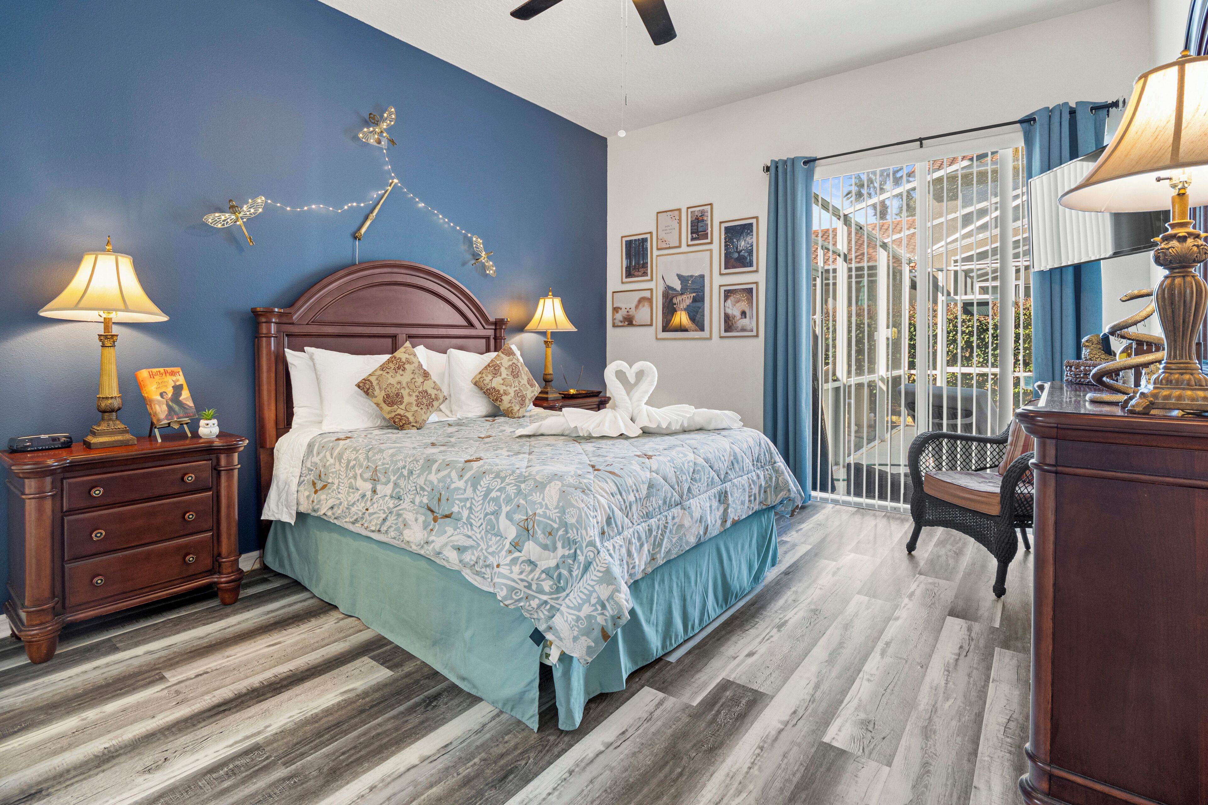 Un dormitorio con una cama de madera, dos mesitas de noche con lámparas, un ventanal con cortinas y vistas al exterior.