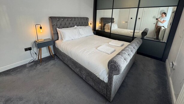 A modern bedroom with a large bed, bedside tables, a mirror, and a hanging light fixture.
