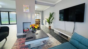 A modern living room with a flat-screen TV mounted on the wall, a coffee table with a vase of flowers, a sofa, and a fireplace.