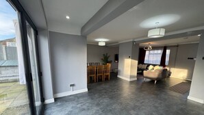 A spacious living area with a large sliding glass door, a dining table with chairs, a sofa, and a chandelier.