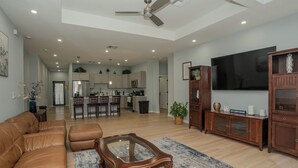 Un ampio soggiorno con un divano in pelle marrone, un tavolino in vetro e un mobile in legno. Una grande TV a schermo piatto è montata a parete e c'è una ventola a soffitto.