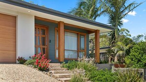 Ein modernes Haus mit überdachter Veranda, einem Kiesweg und verschiedenen Pflanzen.
