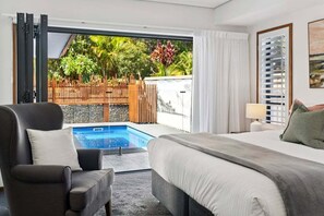 A hotel room with a bed, a chair, a desk, and a view of a swimming pool and outdoor area. - La Playa - Sleeps 10, Pet Friendly, Pool, Gym, Fire pit & room for the whole crew (Coffs Harbour)