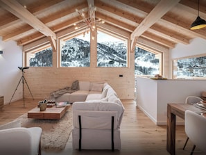 Un loft espacioso con techo alto, vigas de madera, una zona de estar acogedora y ventanas amplias con vistas a la montaña.