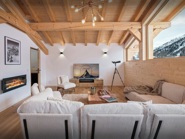 A cozy living room with a fireplace, comfortable seating, a large window with a view of a snowy landscape, and a mounted telescope.