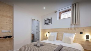Une chambre à coucher bien rangée, avec une tête de lit en bois, un grand lit recouvert de linge de lit blanc, une table de chevet avec une lampe et une fenêtre avec des rideaux.