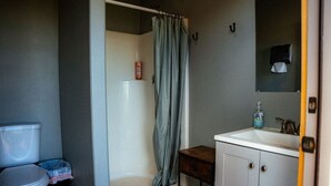 Un baño con inodoro, ducha con cortina, lavabo con dispensador de jabón y un mueble.