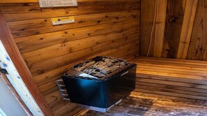 Una sala de sauna con paredes de madera, un calentador de sauna negro y un letrero de precaución.