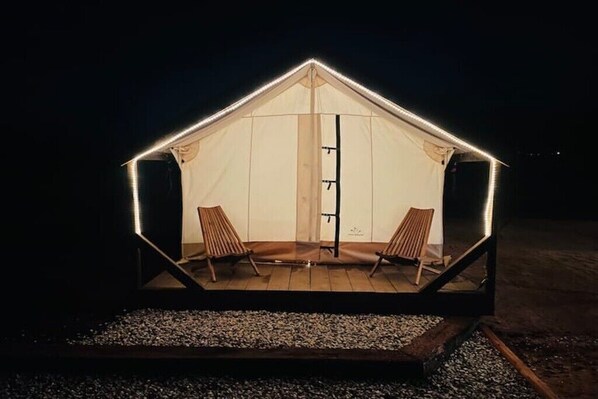 A tent-like structure with two wooden chairs inside, a central pole, and a gravel base.