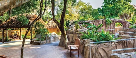 A wooden deck with a bench, surrounded by tropical vegetation and rock formations.