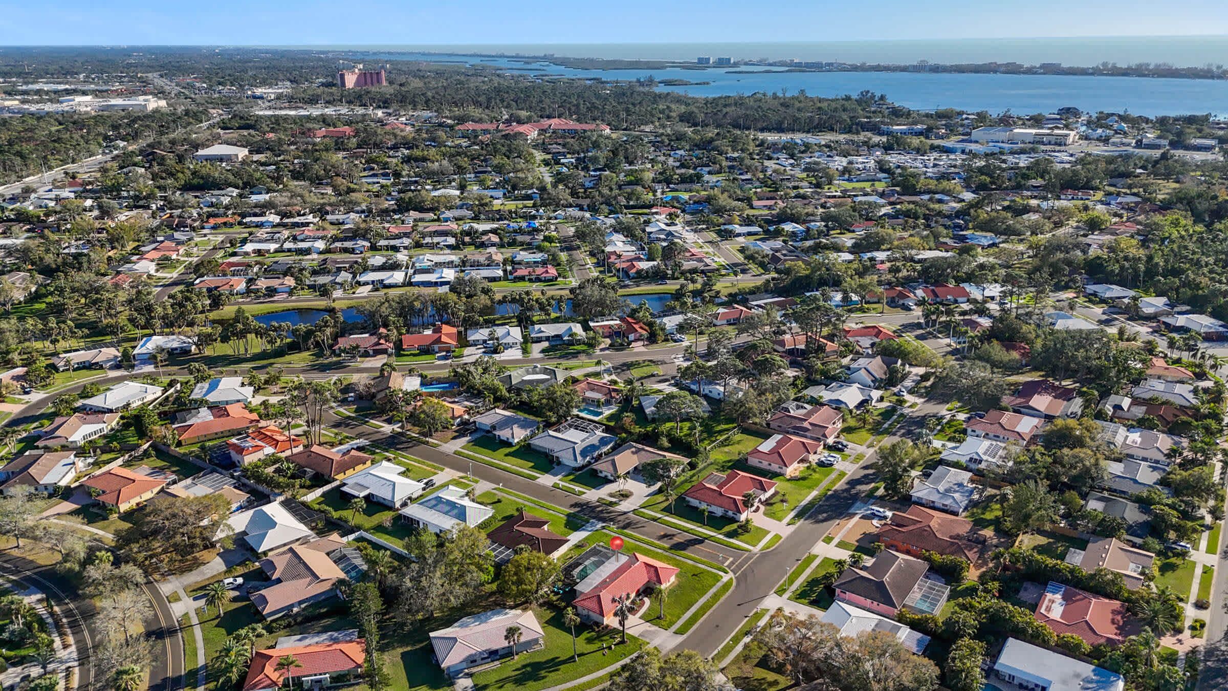 An aerial view of a residential area with houses, roads, and a large body of water in the background.