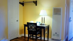 Een kleine kamer met een witte deur, een tafel met een lamp, een stoel en een witte airconditioner.