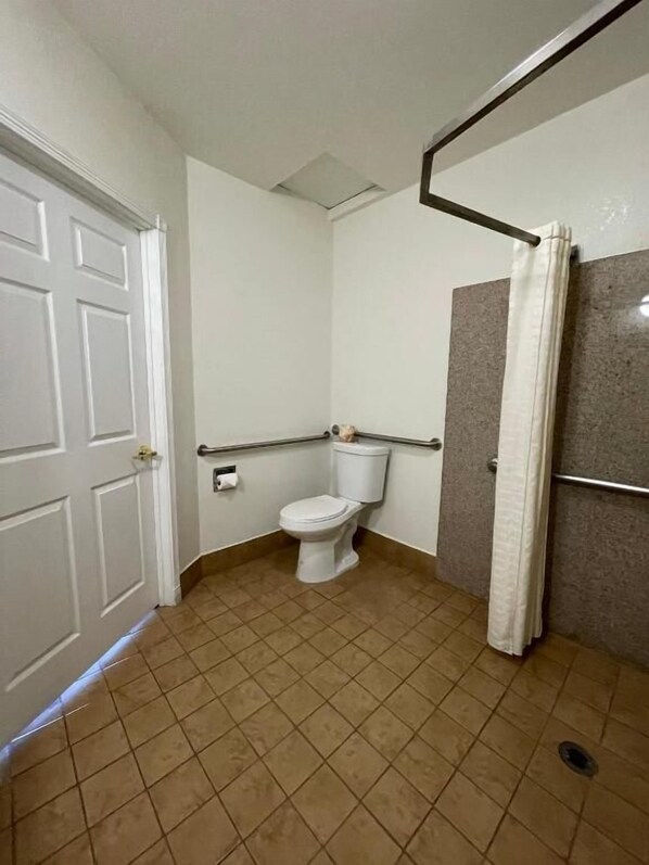 A bathroom with a toilet, a shower, and a door. - Palm Tropics Motel (Glendora)