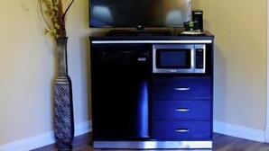 Een hoekappartement met een flatscreen televisie op een zwarte dressoir, een magnetron en een vaas met gedroogde planten.