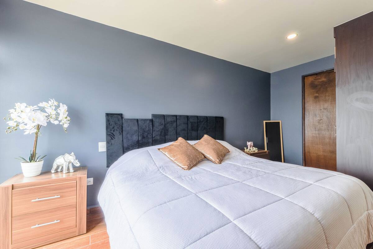 A bedroom with a large bed, a nightstand, a dresser, a mirror, and a door.