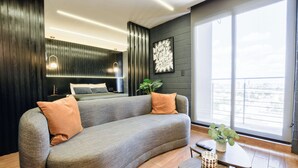 A modern living room with a grey sofa, a small table with a plant, and a bed with a dark headboard. - Barrio Vergel (Monterrey)