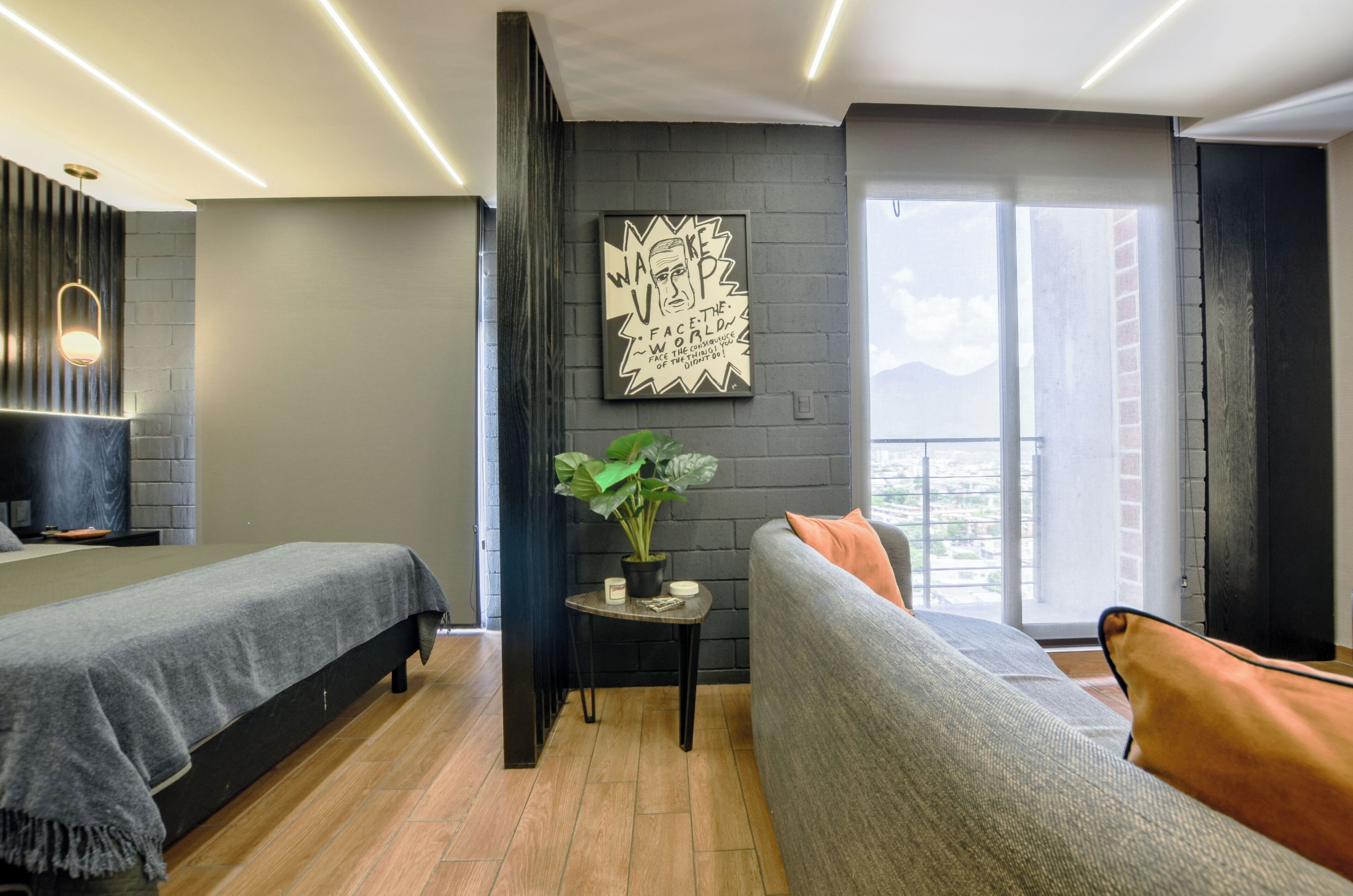 A modern hotel room with two beds, a grey sofa, a small table with a plant, and a large window with a view.
