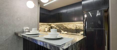 Cozinha moderna com bancada de mármore, armários pretos e geladeira de aço inoxidável.