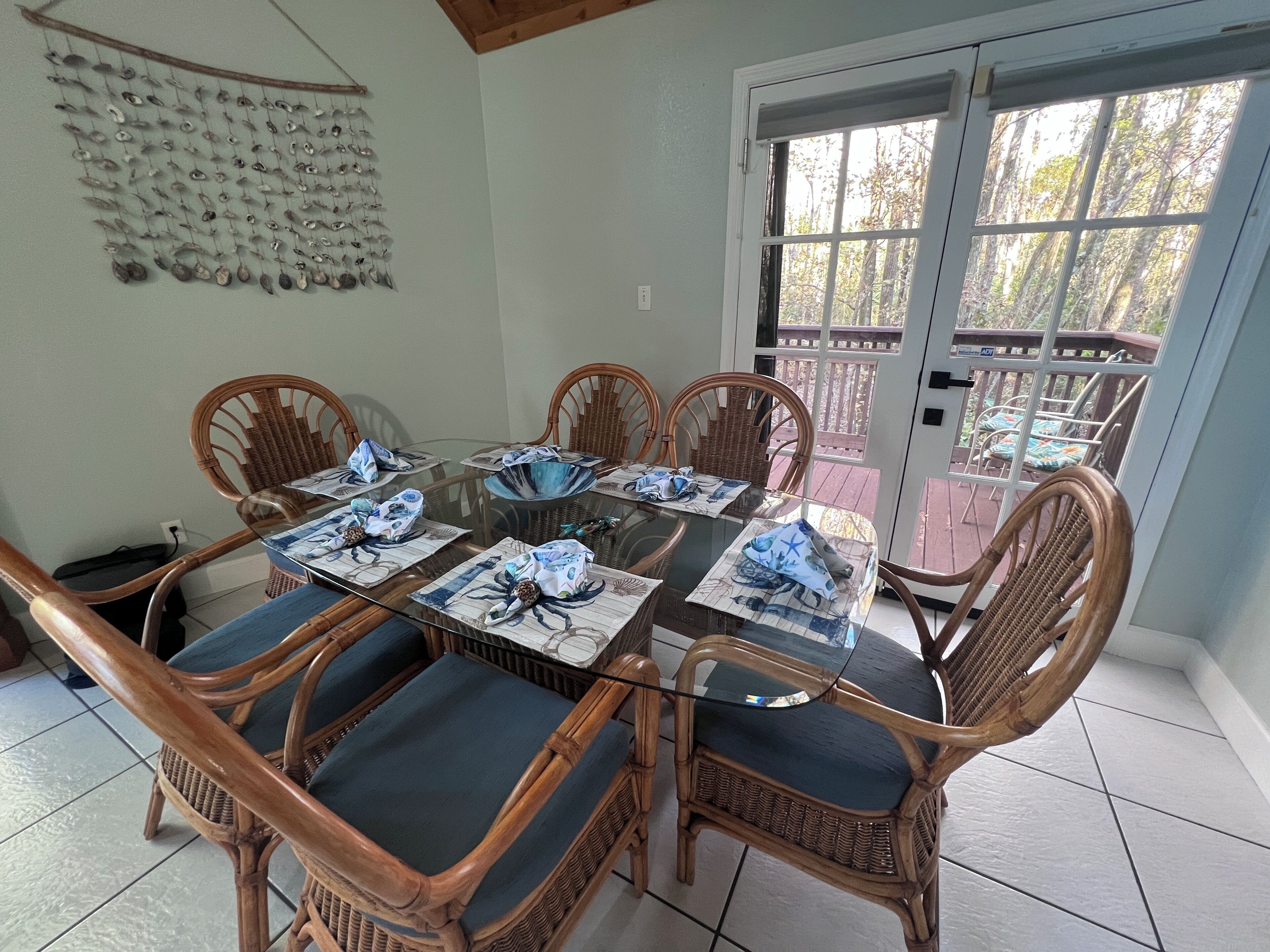 Un comedor con una mesa de vidrio rodeada de sillas de mimbre con cojines azules.
