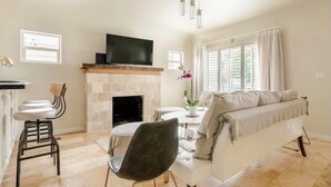 Un salon avec une cheminée, un canapé, un téléviseur fixé au-dessus de la cheminée et un coin repas comprenant une table et des chaises.