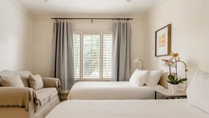 Une chambre d’hôtel avec deux lits, un canapé, une petite table avec une lampe et une fenêtre avec des rideaux.