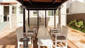 Une terrasse extérieure dotée d’une pergola en bois, de mobilier blanc et offrant une vue sur les bâtiments voisins.