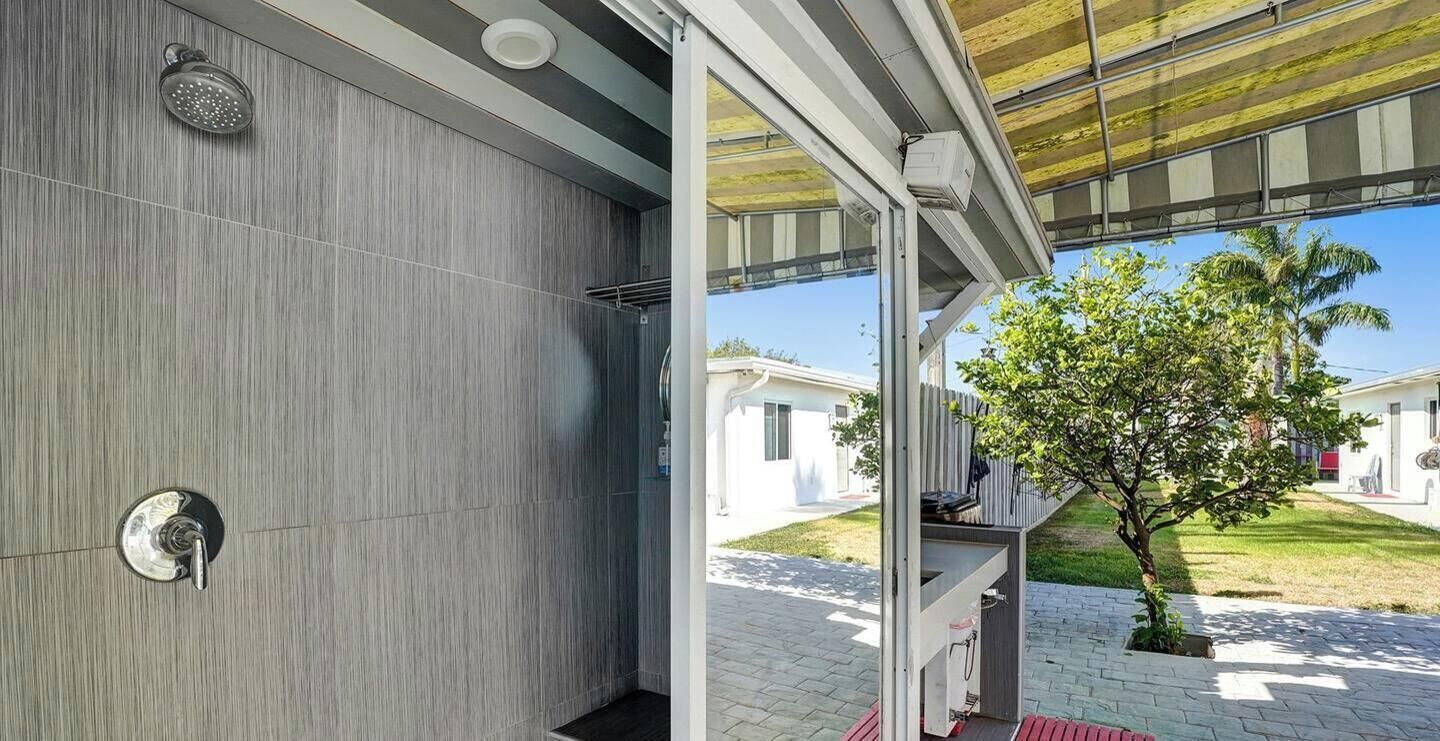 Un baño moderno con ducha, toallero y puerta de vidrio que da a un espacio exterior con un árbol y un camino.