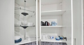 Cozinha com armários brancos, uma prateleira de vidro com utensílios de cozinha e uma cafeteira.