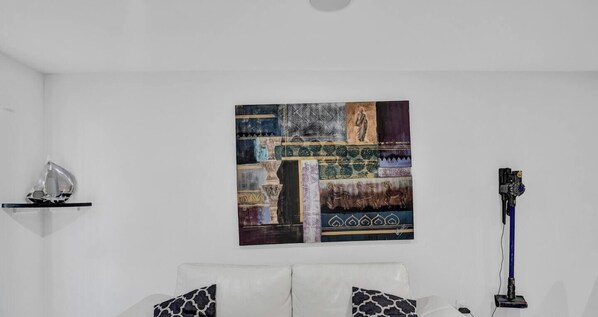 Quarto com parede branca, pintura, sofá branco com almofadas estampadas e abajur.