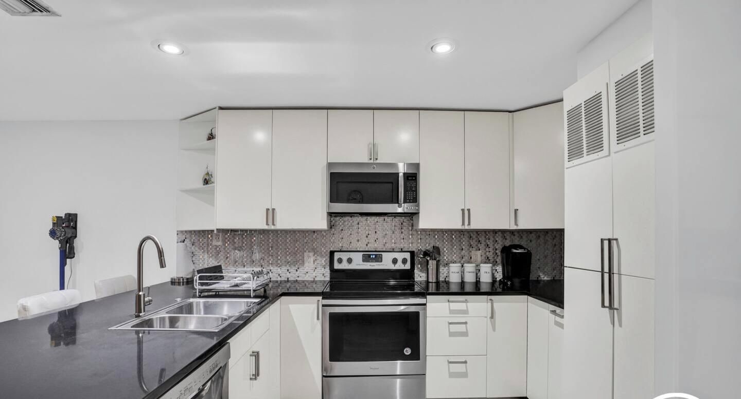 A modern kitchen with white cabinets, stainless steel appliances, and a black countertop.