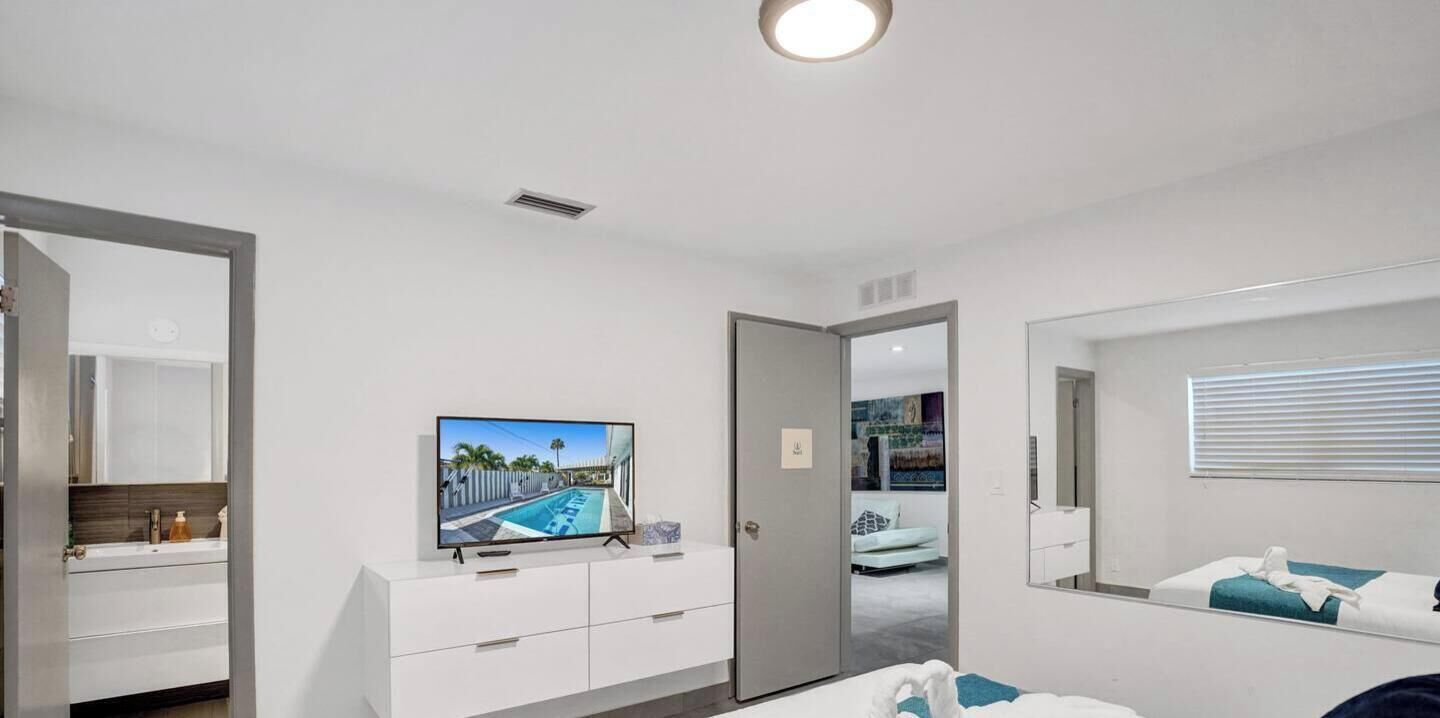 Ein modernes Hotelzimmer mit großem Flachbildfernseher, begehbarem Kleiderschrank, Badezimmer mit Spiegel und einem Bett mit blauem Akzent.