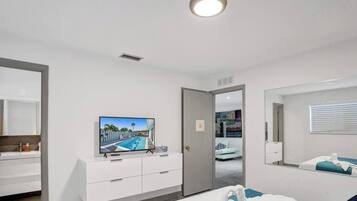 Ein modernes Hotelzimmer mit großem Flachbildfernseher, begehbarem Kleiderschrank, Badezimmer mit Spiegel und einem Bett mit blauem Akzent.