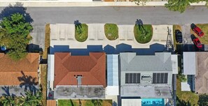 Vista aérea de um estacionamento com vários carros, um edifício com telhado vermelho e áreas verdes ajardinadas.