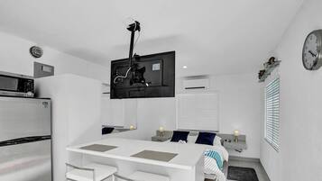 Een compacte hotelkamer met kitchenette, een flatscreen televisie aan de wand, een bed met nachtkastje en een bedtafel.
