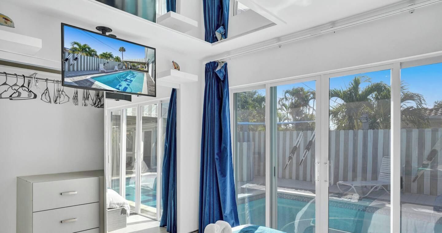 Ein Hotelzimmer mit Fernseher, einer Schiebetür zum Pool und einer weißen Kommode.