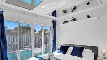 Une chambre d’hôtel comprenant un lit, une table de chevet, une lampe, une fenêtre avec des rideaux et une vue sur une piscine et un espace extérieur.