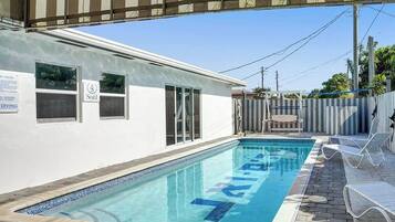 A swimming pool with a covered area, a fenced backyard, and a building with windows.