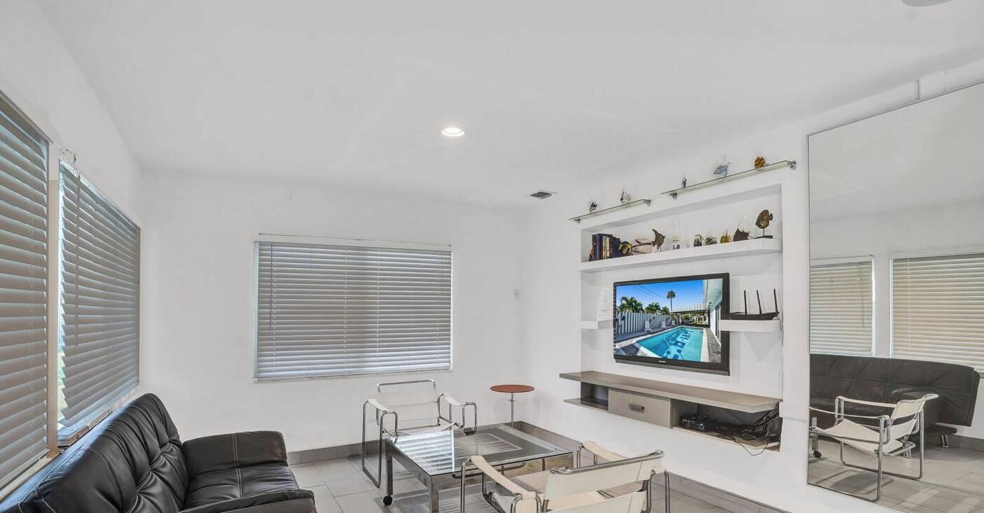 A modern living room with a flat-screen TV, a sofa, a coffee table, and a glass-top dining table.
