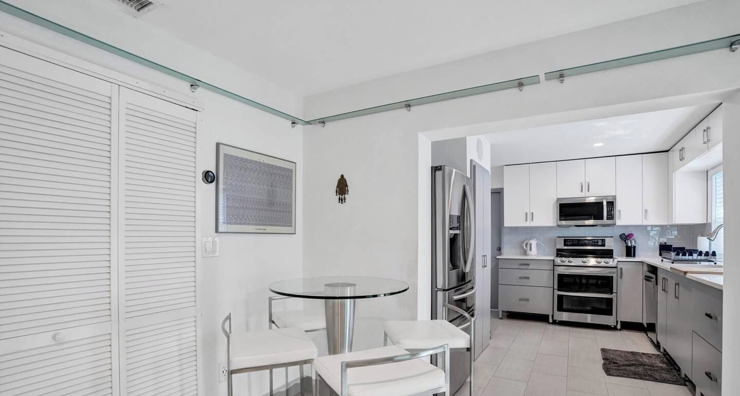 A compact kitchen with modern appliances, a glass table, and white cabinetry.