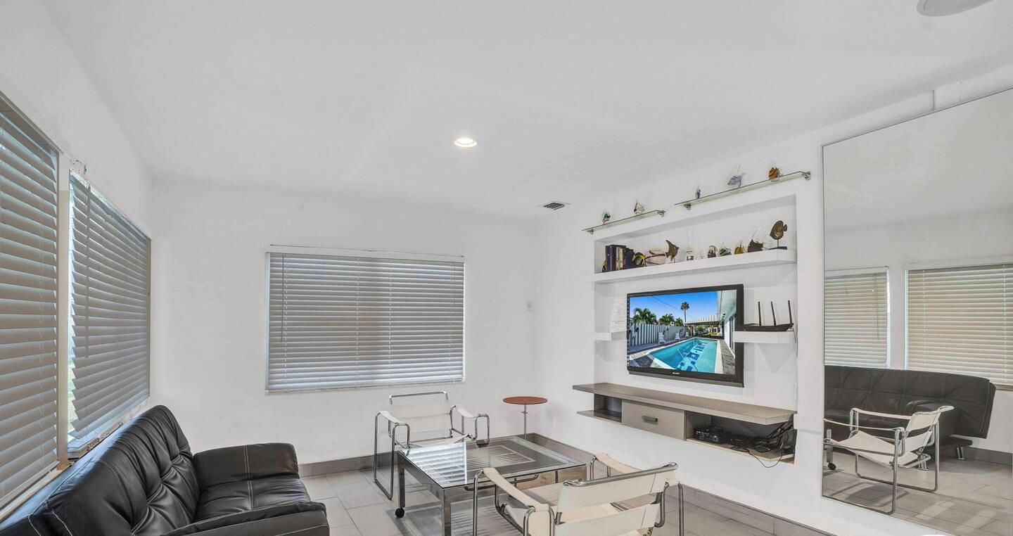 Un salon moderne avec un canapé, une table basse en verre, un téléviseur fixé au mur et une bibliothèque agrémentée d’objets décoratifs.